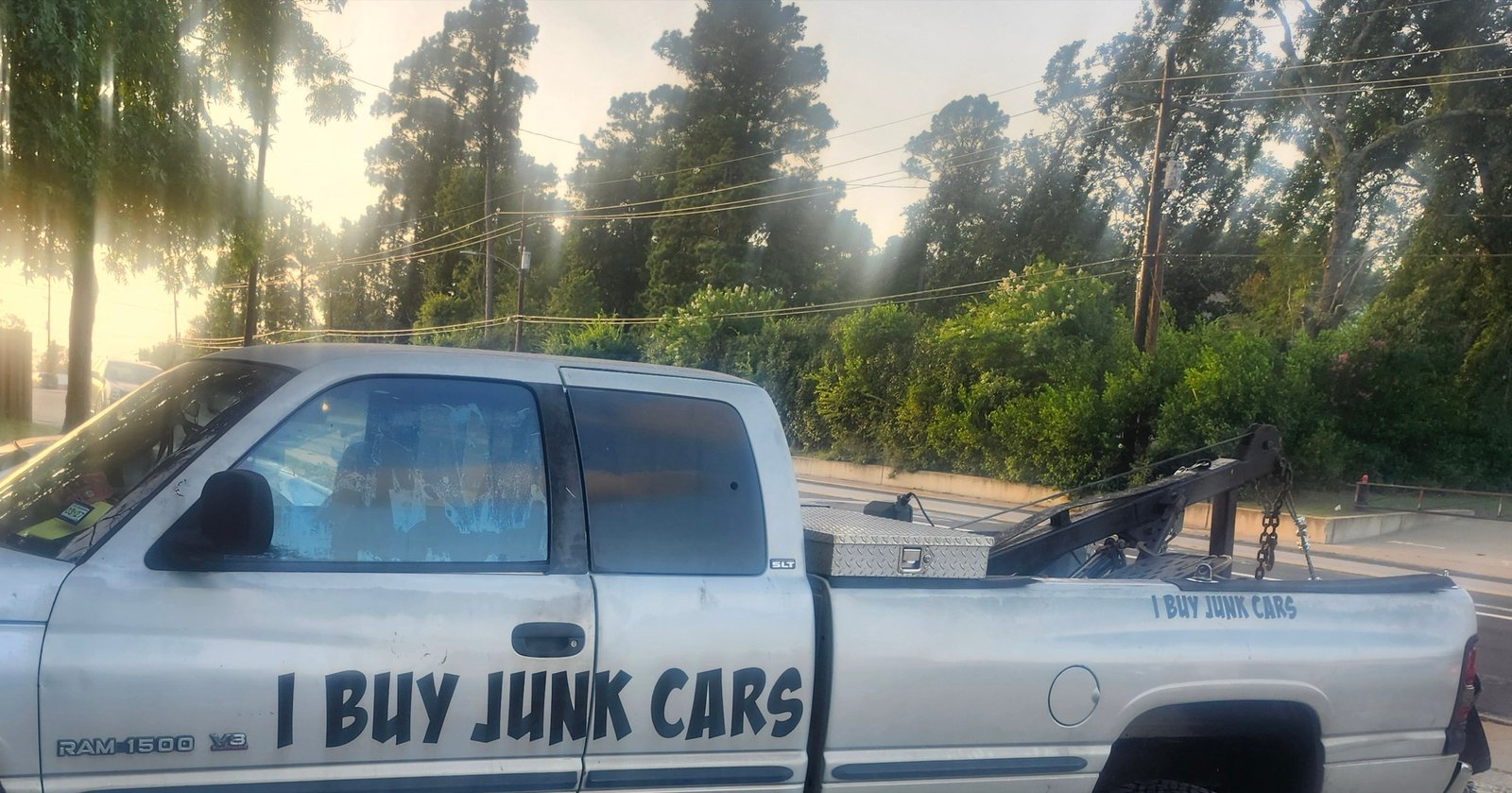 A white pickup with a tow boom parked at sunrise, &lsquo;I Buy Junk Cars&rsquo; lettered along the door.